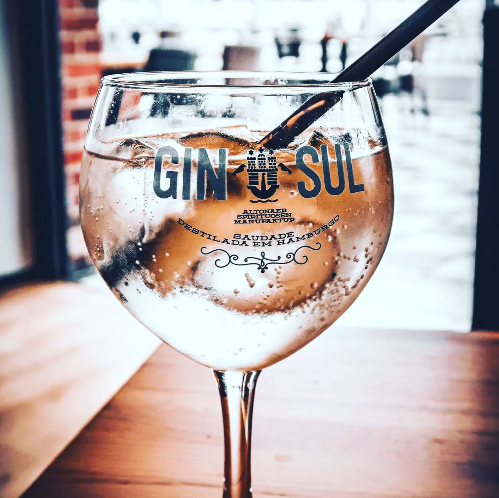 Gin Tonic im bauchigen Gin-Sul-Glas mit Eiswürfeln, dahinter die Backsteinwand im Fischermänns.