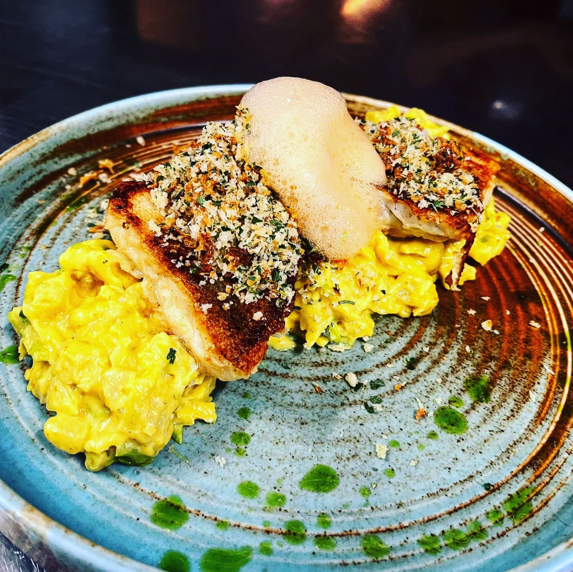 Gebratenes Fischfilet mit Kräuterkruste auf cremigem Risotto, garniert mit Schaum, auf handgetöpfertem Teller.